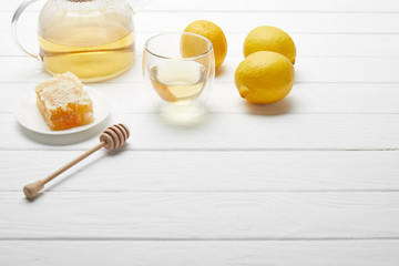 transparent teapot and glass with green tea, lemons, honeycomb and wooden honey dripper on white table