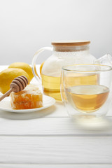 teapot with organic herbal tea, glass, lemons and honeycomb on white wooden table
