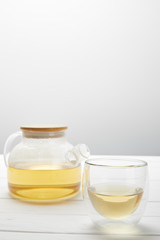 teapot with organic herbal tea and transparent glass on grey with copy space