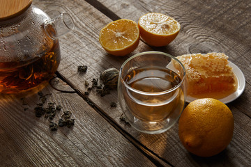 lemons, honeycomb and transparent teapot with glass of traditional chinese blooming tea on wooden table