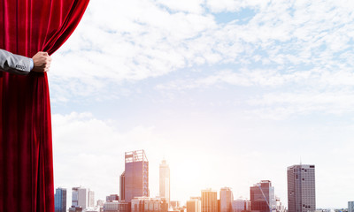 Modern business cityscape behind curtain opened by businessman hand