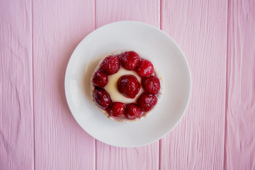 panna cotta brownie with large fresh raspberries stands on a saucer in the center of the frame on a pink wooden background close-up