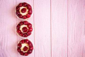 several appetizing beautiful bright panna cotta cakes in baskets with berries on a pink wooden background on the left of the frame and a large space for text on the right