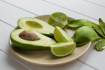 On the plate lies peeled avocado and lime slices, and next to the plate avocado peel