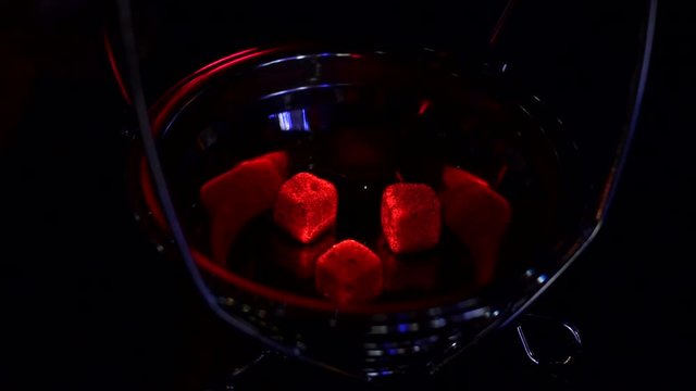Kindling of square coal for a hookah on a special furnace with a hot spiral. Close-up of kindling coals for hookah in hookah bar. Man holds red-hot coal with tongs.