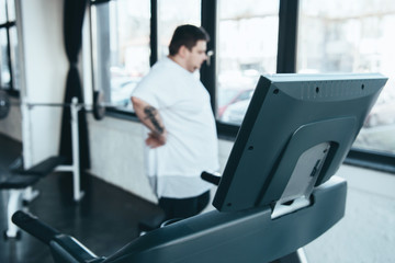 selective focus of treadmill and overweight man looking through window at sports center