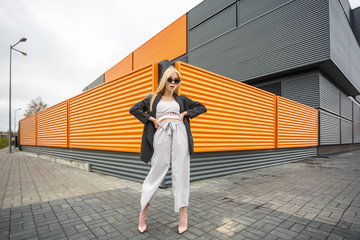 closeup portrait of cute smiling little model girl in striped jacket and sunglasses posing near gray corrugated striped orange gray wall