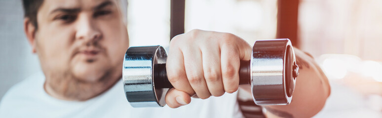 panoramic shot of Overweight man Looking At Camera while training with dumbbell at gym