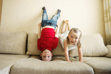 Brother and sister playing on the couch: the boy stands upside down