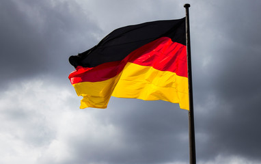 German waving flag in the cloudy sky on the background. Nation, culture, patriotism.