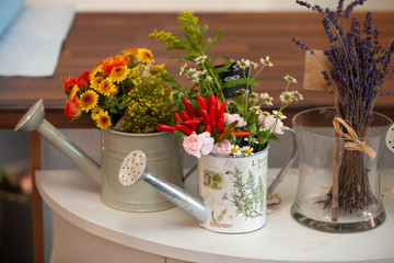 Mixed coloured wild flowers arranged in watering cans and a glass vase
