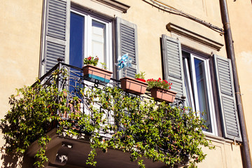 Fototapeta na wymiar Beautiful charming pair of windows with shutters on a facade of residential building with green balcony and flowers on it in Bergamo Italy.