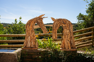 Two wooden horses heads made of driftwood in a garden during the summer