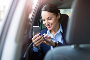 Young businesswoman on the back seat of a car with smart phone