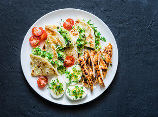 Large tapas plate - grilled, chicken, avocado cream cheese quesadilla, boiled eggs, vegetables - tasty snack on a dark background, top view
