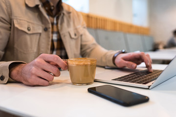 Cropped view of freelancer with cup of coffee typing on laptop keyboard