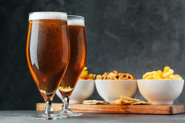 Glass of lager beer with snack bowls on dark stone background