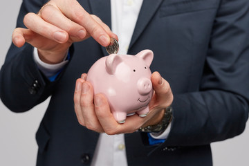 Crop businessman putting coin inside piggy bank