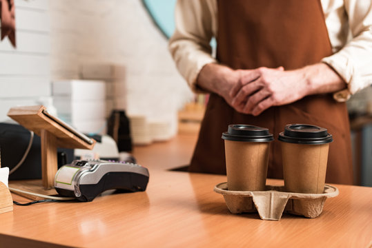 Cropped View Of Barista In Brown Apron And Disposable Cups Of Coffee