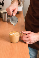 Fototapeta na wymiar Cropped view of barista pouring milk in coffee
