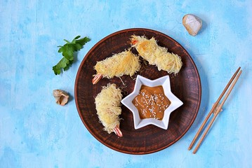 Snack or lunch, large shrimp in a crispy dough Kataify on a clay plate. Served with peanut sauce. Asian cuisine. Top view, copy space.