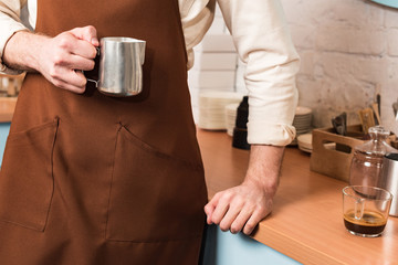 Cropped view of barista holding steel milk jug