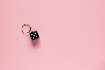 top view of black dice on key chain on pink background. Minimal flat lay concept