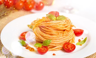 Spaghetti pasta with cherry tomatoes and basil leaves on white plate