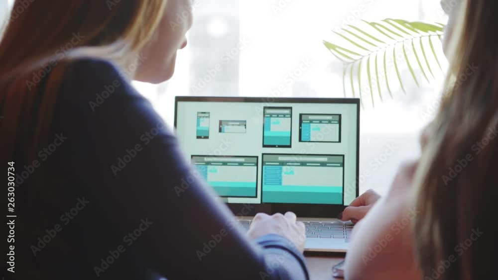 Wall mural rear view of two unrecognizable female professionals discussing website design for different devices