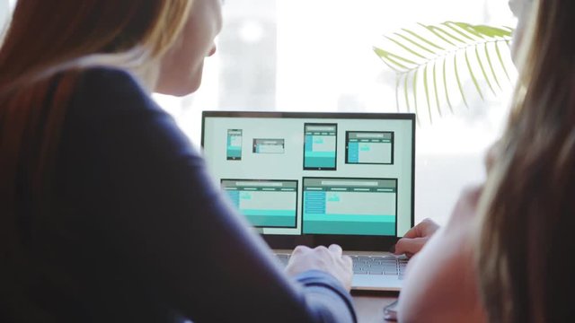Rear view of two unrecognizable female professionals discussing website design for different devices presented on laptop screen sitting at desk (ATTN templates designed by ME)