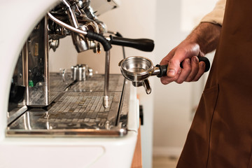 Partial view of barista holding portafilter near coffee machine