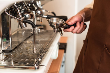 Partial view of barista holding portafilter near coffee machine