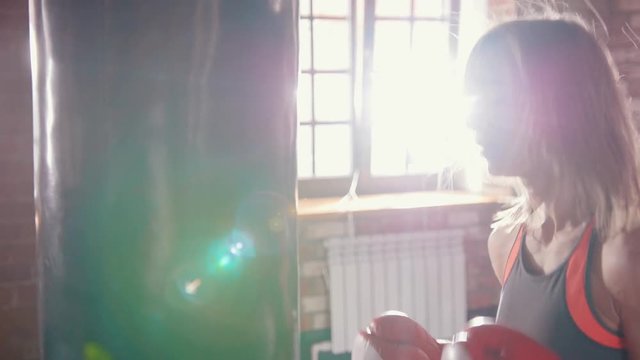 A woman boxer hitting the punching bag in the gyn. Sun comes from the window