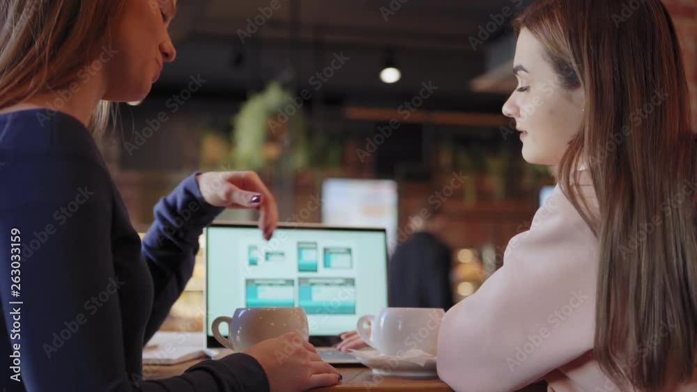 Wall mural side view of two young businesswomen discussing website design for different devices presented on la
