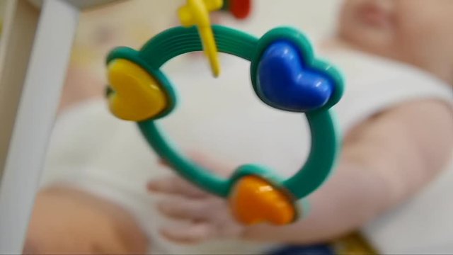 Kid lying on bed with rattle. Infant playing baby rattle.