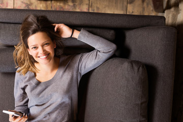 Obraz premium Beautiful and happy young woman with smartphone smiling on sofa