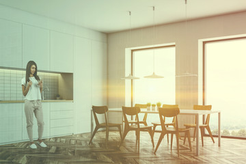 Woman with phone in white kitchen with table
