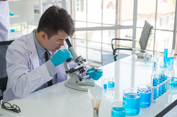 scientists working at the research center using a microscope. chemists working with blue liquids in...
