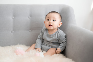 Baby girl is smiling and sitting on sofa in jumpsuit