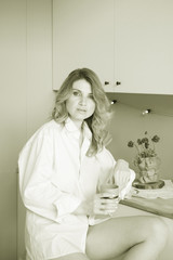 beautiful blonde girl in the kitchen with a cup of coffee or tea in her hands and looking into the camera sepia toned