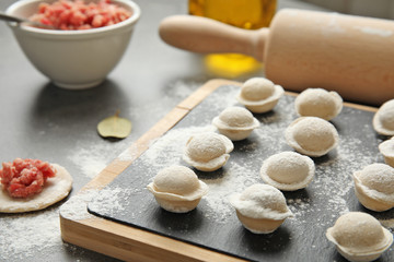 Fototapeta na wymiar Board with raw dumplings on table, closeup. Process of cooking