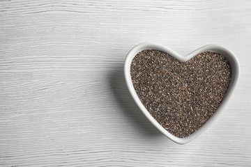 Heart shaped bowl with chia seeds on wooden background, top view. Space for text