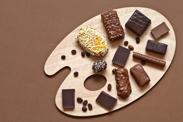 A palette of chocolate tastes. Different types of dark and milk chocolate, sweets and coffee corns on the cutting board in the form of a palette. Top view, flat lay, close up, copy space