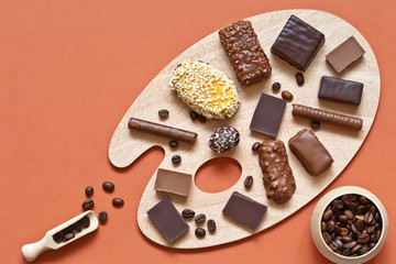 Different types of dark and milk chocolate, sweets and coffee beans on cutting board in form of palette on bright festive table. A palette of chocolate flavors. Top view, flat lay, place for text