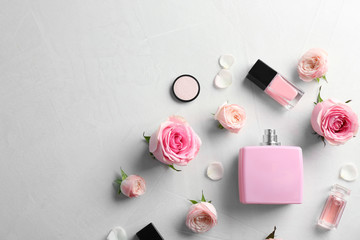 Flat lay composition with bottles of perfume, cosmetics and roses on grey background. Space for text