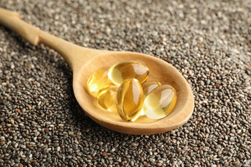 Spoon with oil capsules on chia seeds, closeup