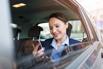 Young businesswoman on the back seat of a car with smart phone