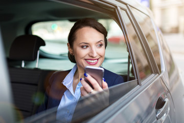 Young businesswoman on the back seat of a car with smart phone