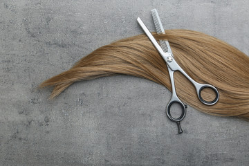 Flat lay composition with light brown hair and thinning scissors on grey background. Hairdresser service