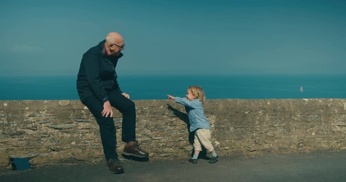 Little toddler having fun with his grandfather by the sea